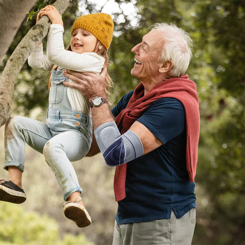 Man lifting a child outdoors while wearing a Bauerfeind EpiTrain elbow support